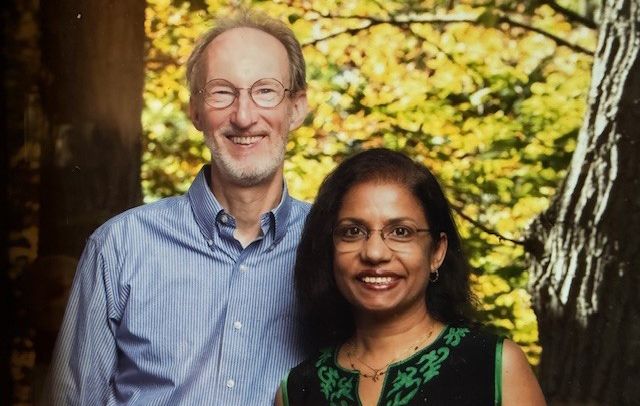 portrait photograph of man and woman standing in front of trees